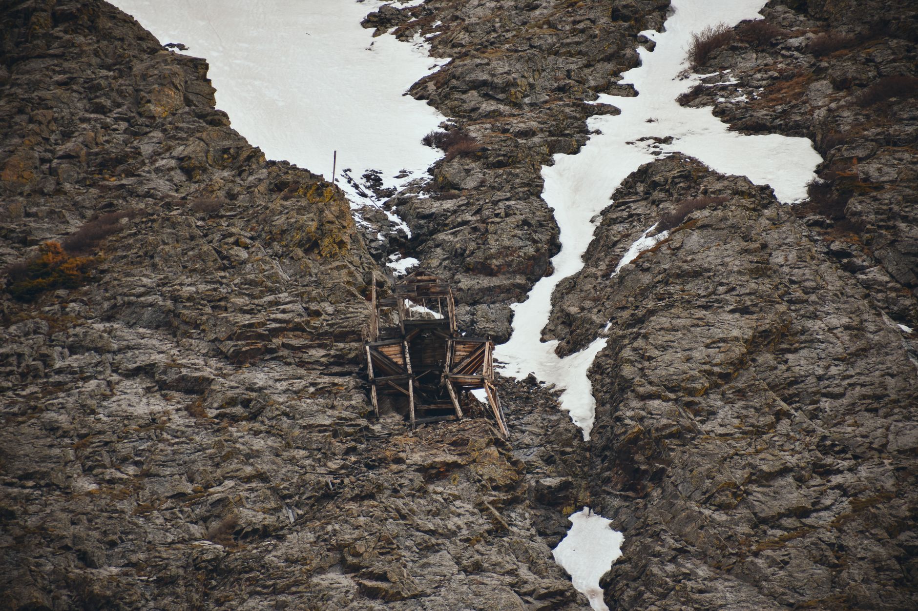 An abandoned mine set against rocky cliffs with patches of snow