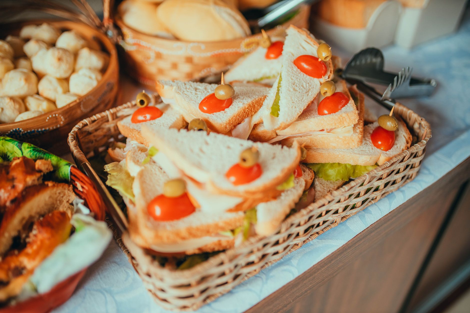 Close-up of assorted sandwiches with olives and tomatoes in a wicker basket