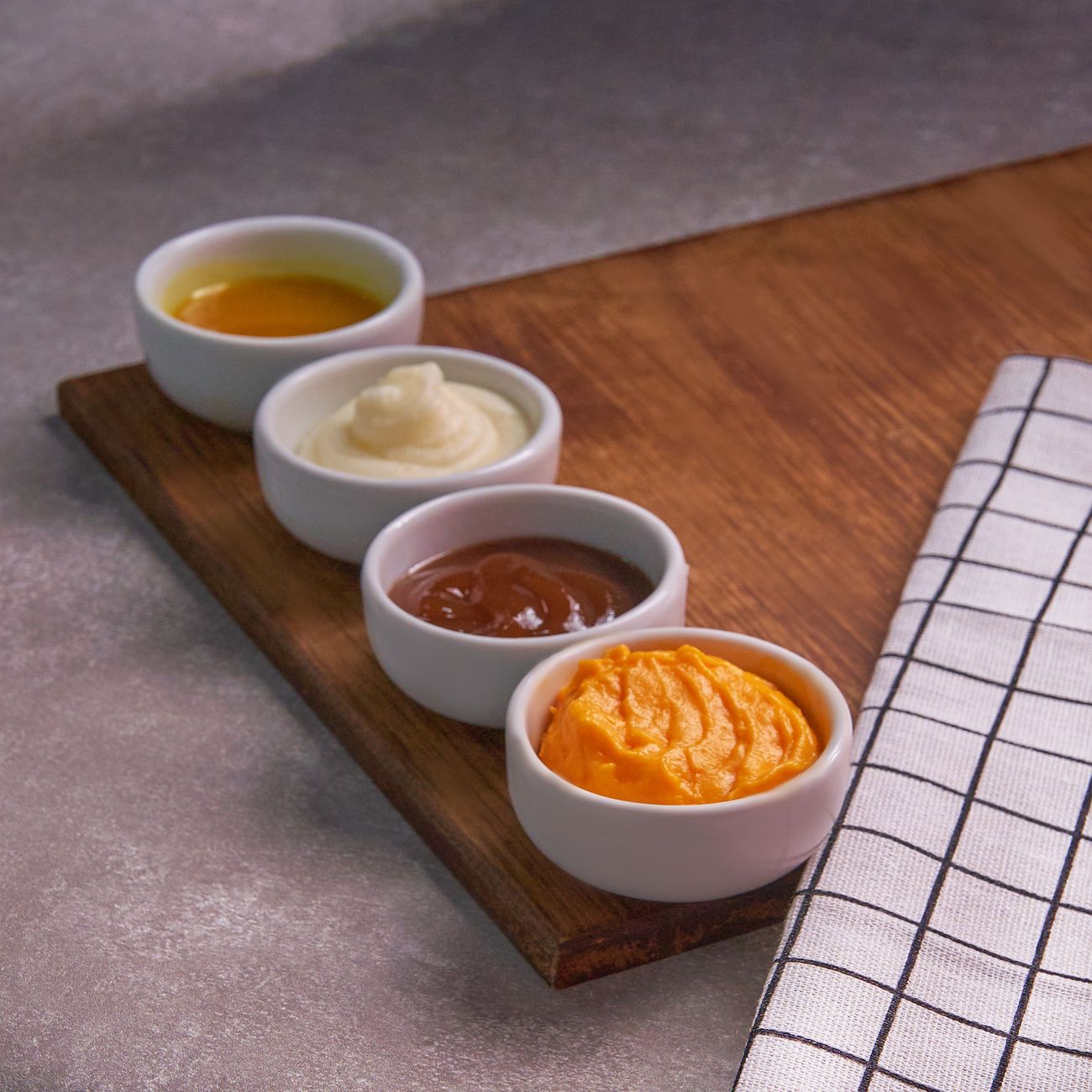 Four assorted sauces displayed in ceramic bowls on a wooden board