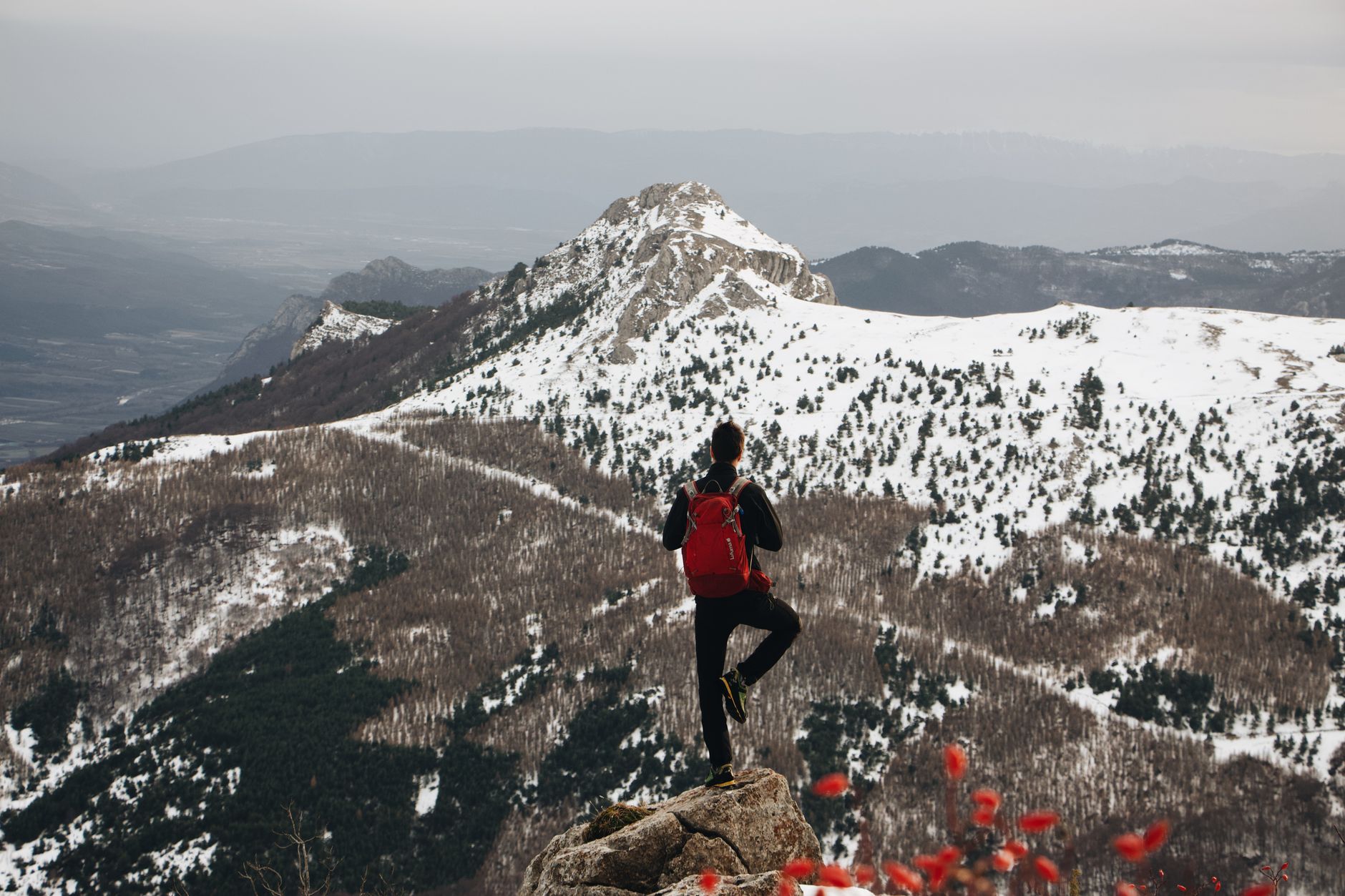 Backpacker stands on a peak, admiring a snow-covered mountain range