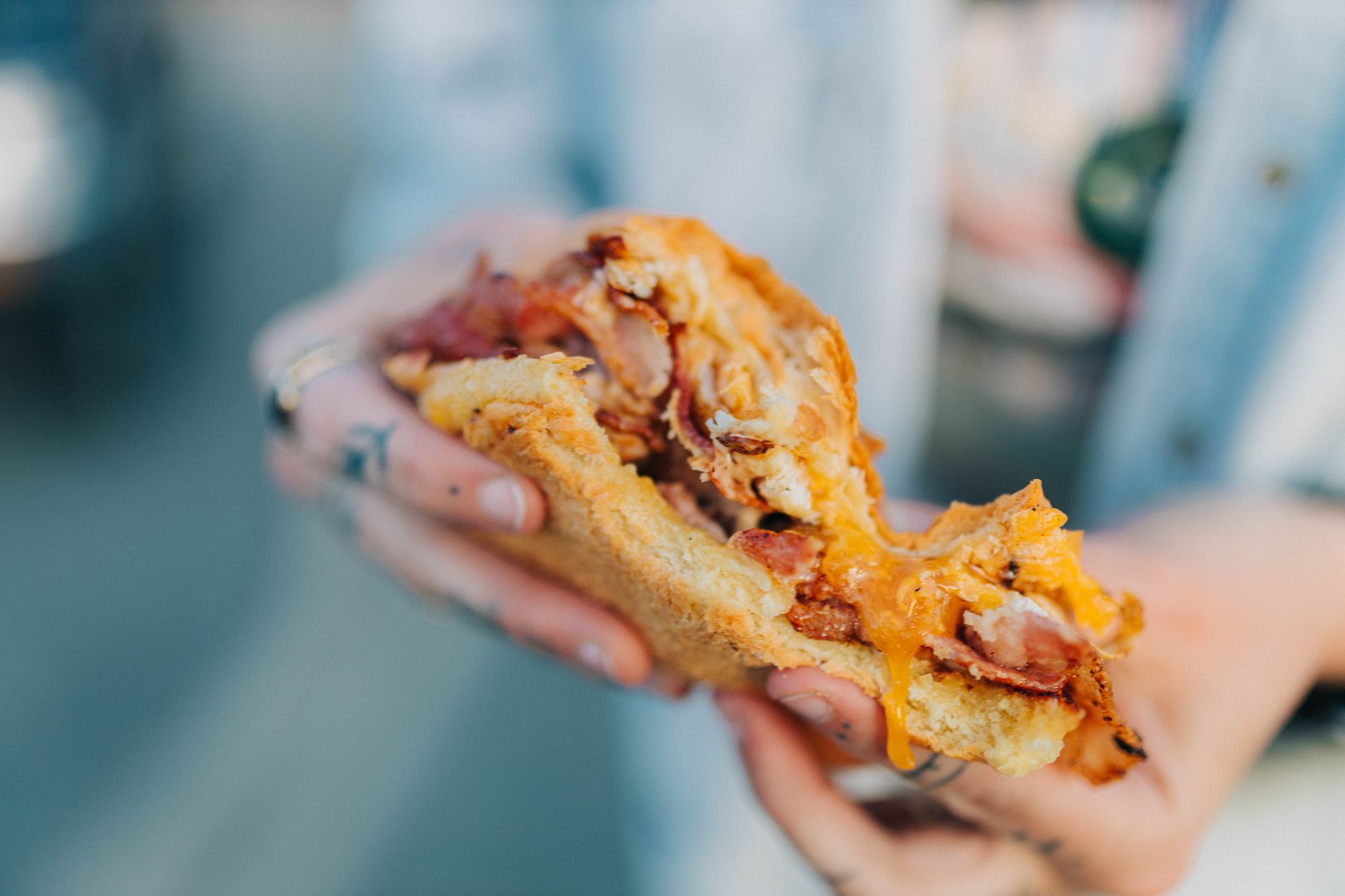 Delicious bacon egg sandwich with melted cheese in hand