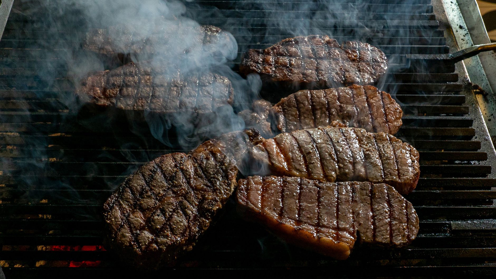 Juicy beef steaks being grilled with smoke rising, perfect for barbecue