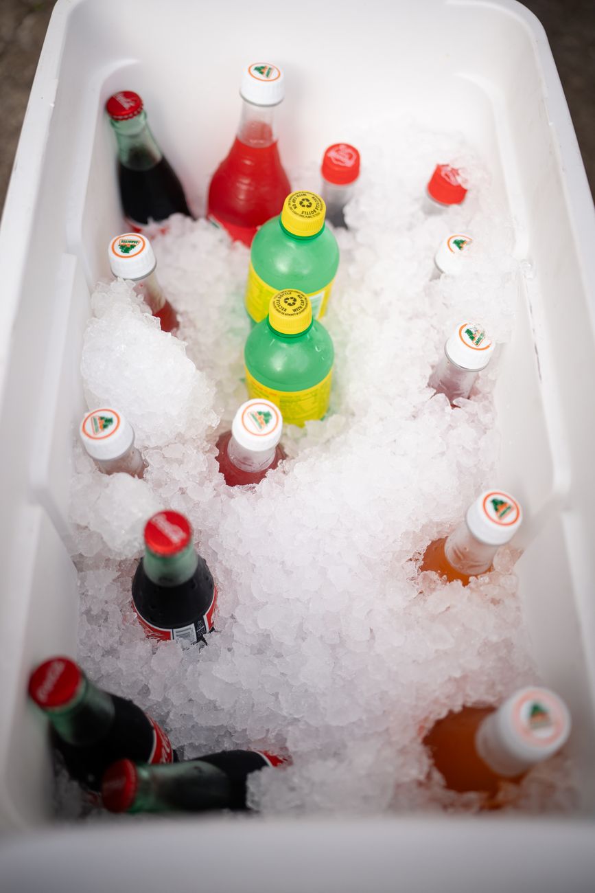 A variety of beverage bottles chilled on ice inside a white cooler