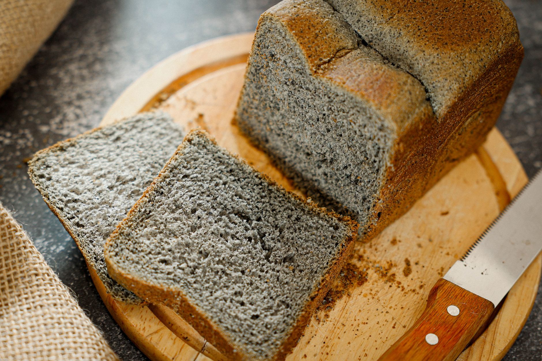 A freshly baked black sesame bread loaf and slices on a wooden board