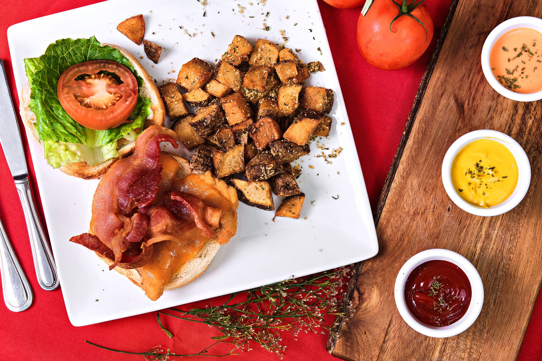Top view of a BLT sandwich with crispy potatoes and dips on a plate