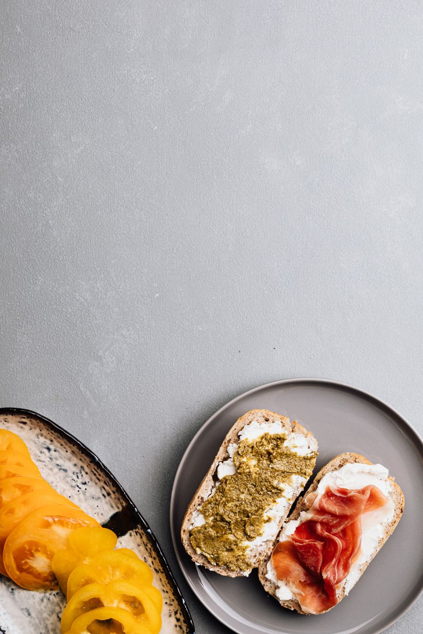 A flat lay of bread slices with pesto and prosciutto on a gray table