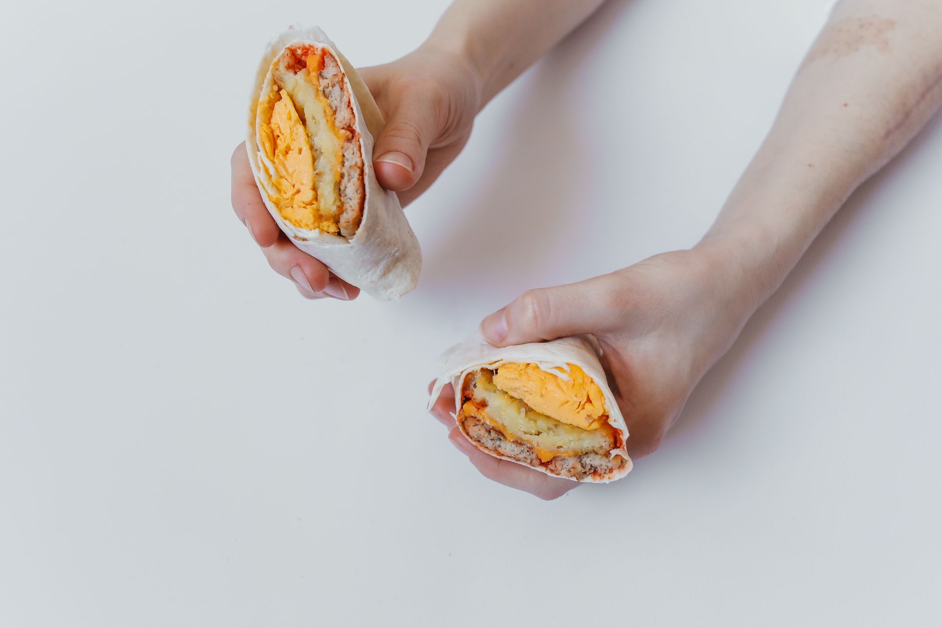 Hands holding a cut breakfast burrito with eggs, cheese, and sauce