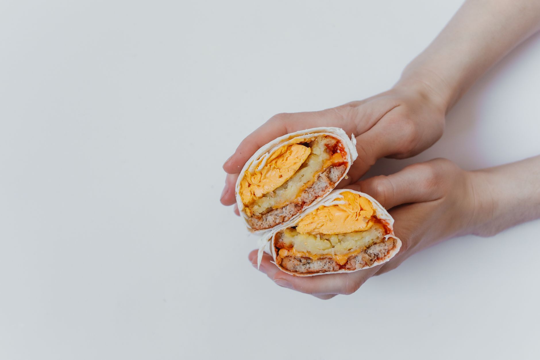 A breakfast burrito with eggs and cheese held by hands