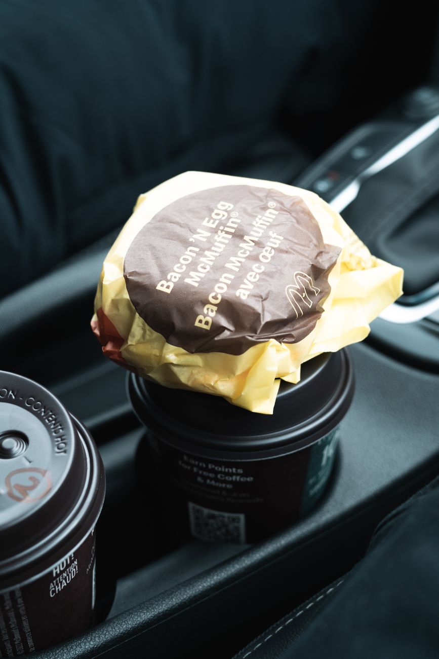 Close-up of a breakfast muffin and coffee cups inside a car