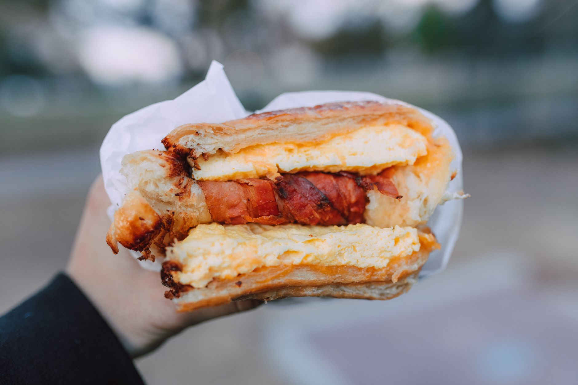 Close-up of a delicious breakfast sandwich with cheese and bacon held in hand