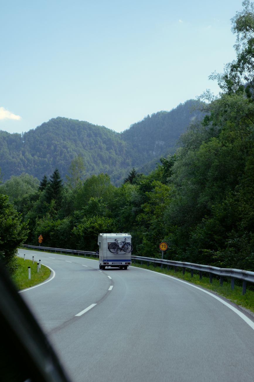 Camper van travels on a winding road surrounded by lush forest and mountains