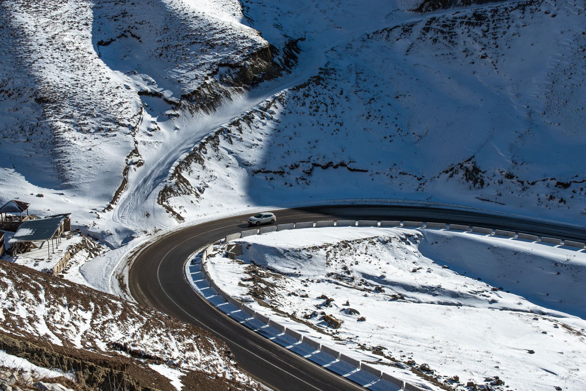 A car navigates a scenic winding road through snow-covered mountains