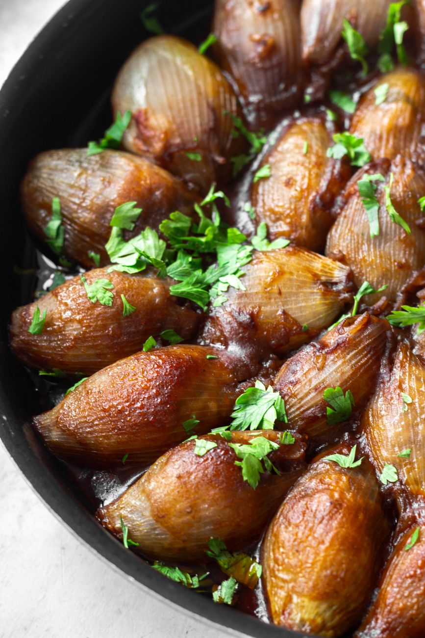 Close-up of caramelized shallots topped with fresh herbs in a skillet