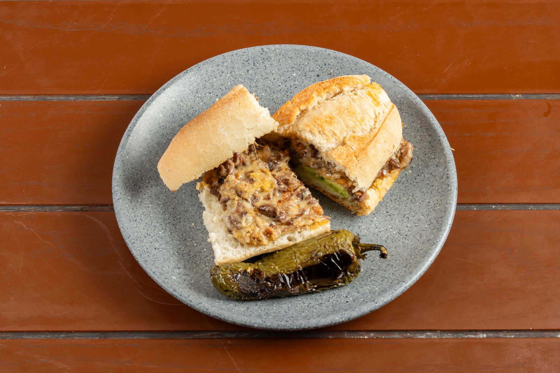A cheesesteak sandwich with grilled peppers on a rustic table