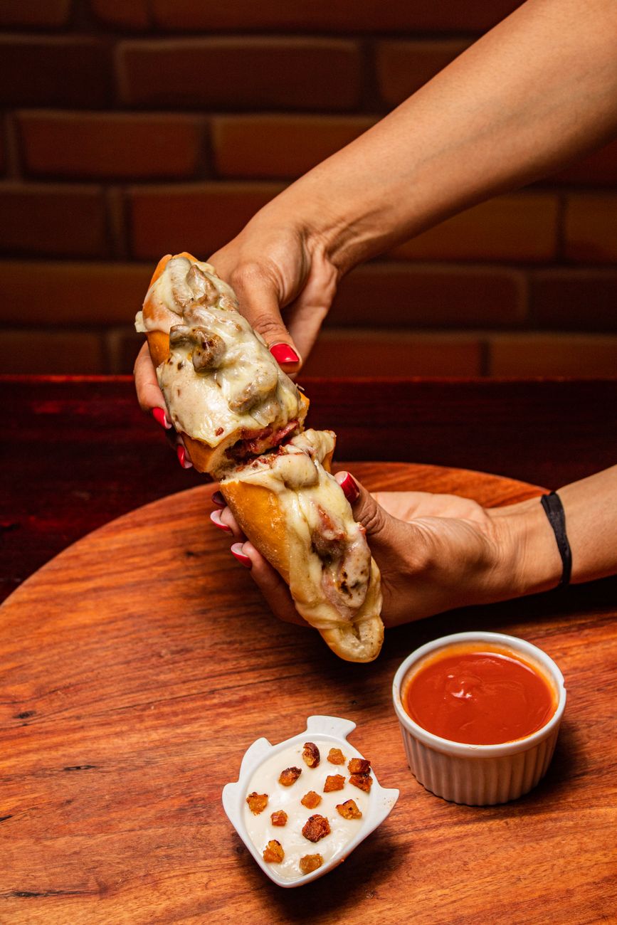 A cheesesteak sandwich with gooey cheese and a side of marinara sauce
