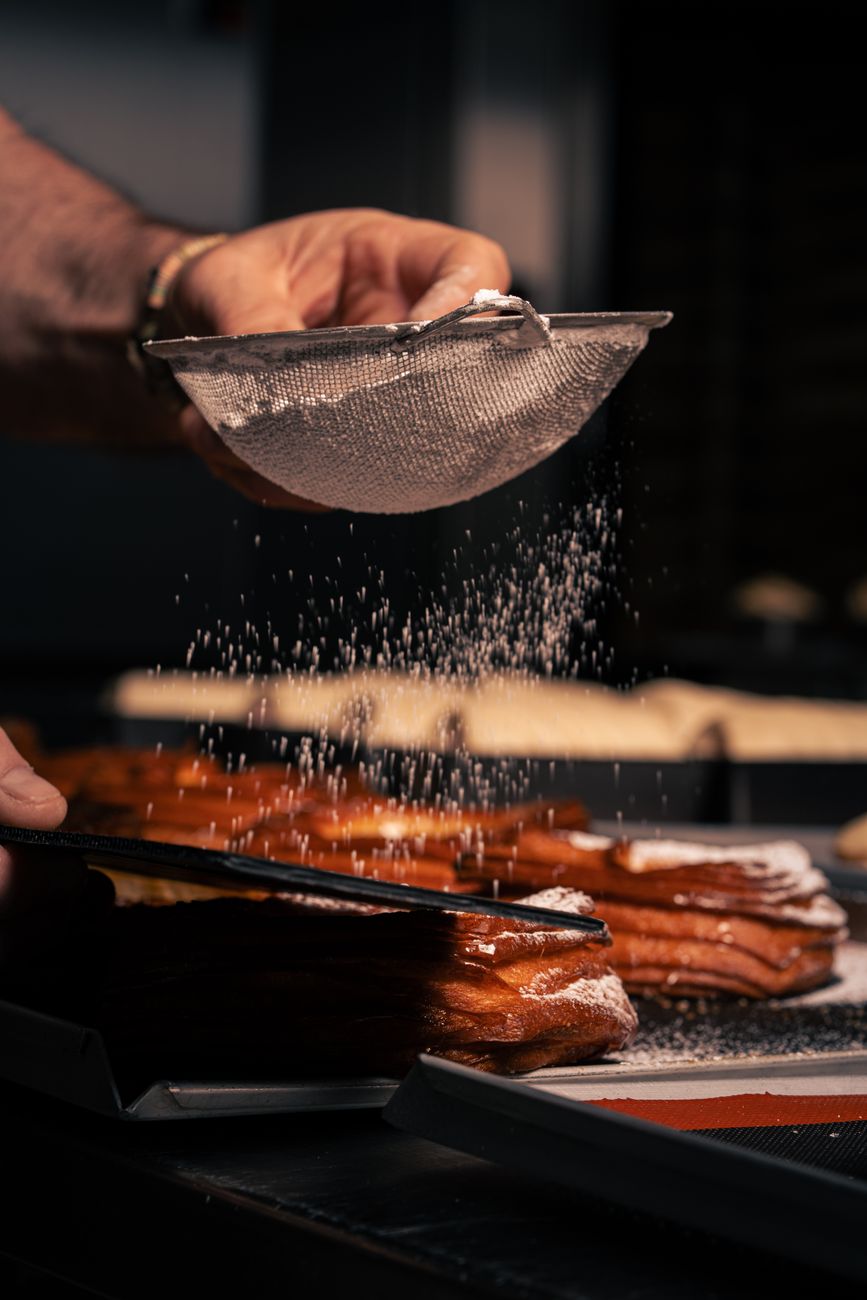 A chef dusting powdered sugar over a pastry in the kitchen