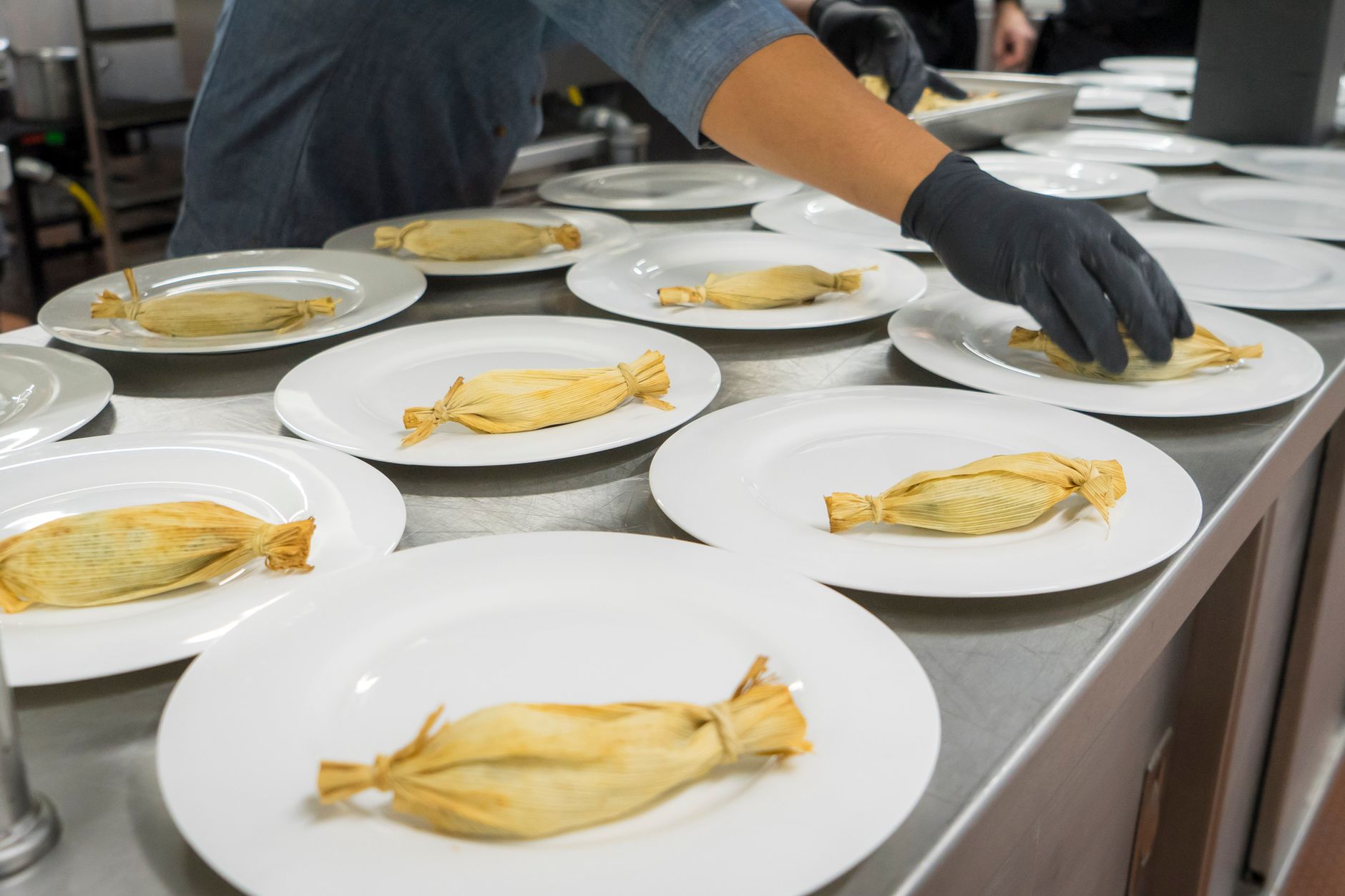 A chef placing tamales on plates in a professional kitchen setting