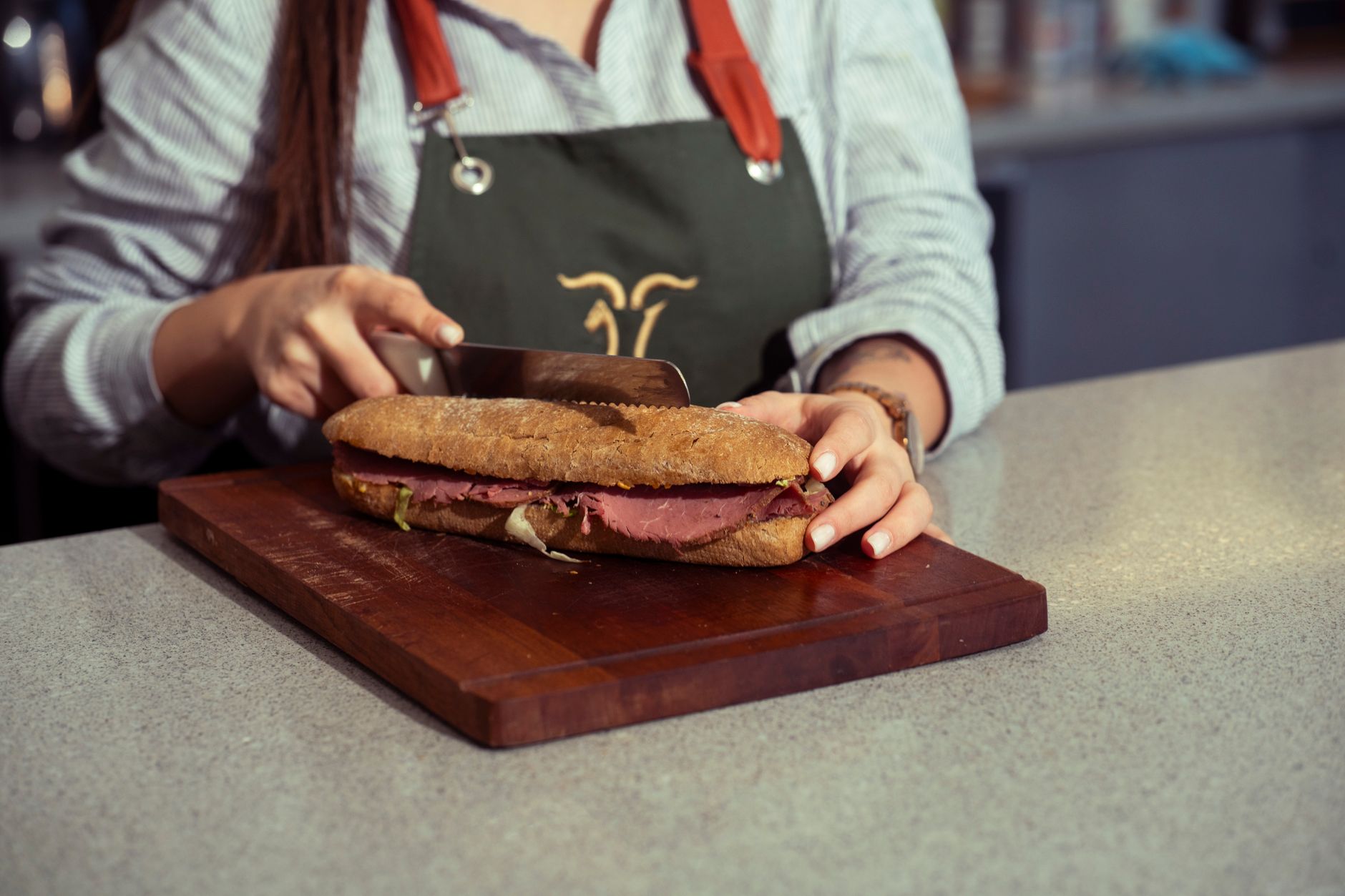 Close-up of a chef slicing a fresh gourmet sandwich on a wooden cutting board