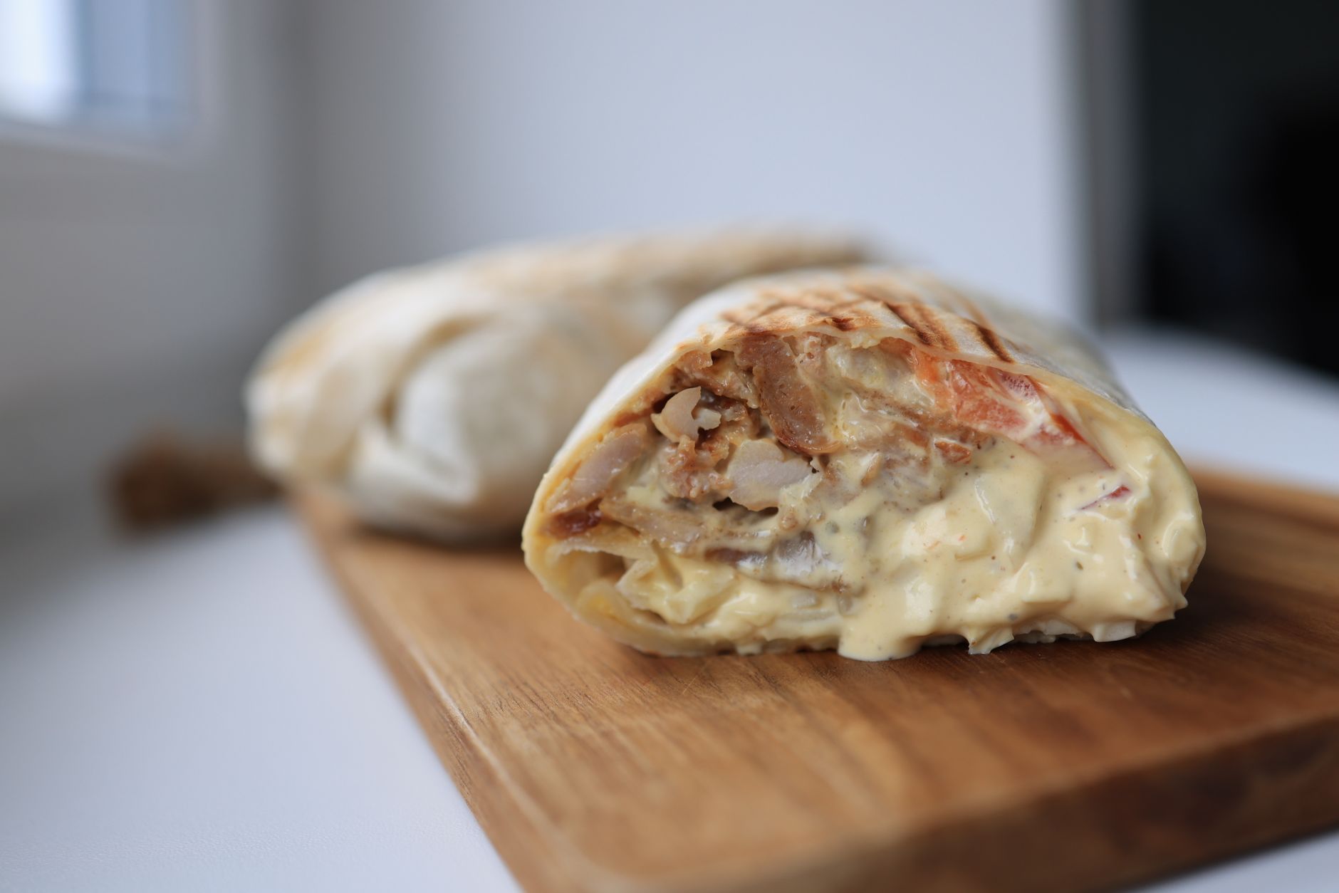 Tasty chicken wrap filled with creamy sauce on a wooden cutting board