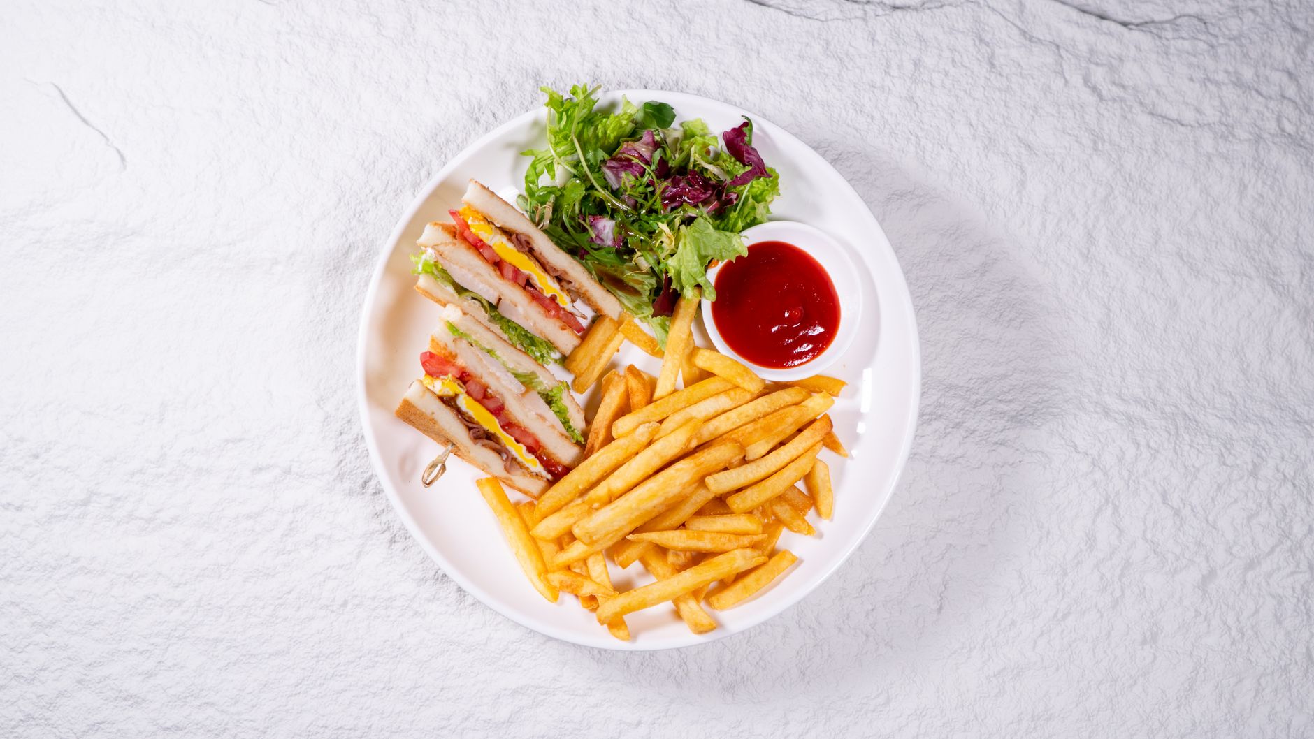 Top view of a club sandwich platter with fries, fresh salad, and ketchup