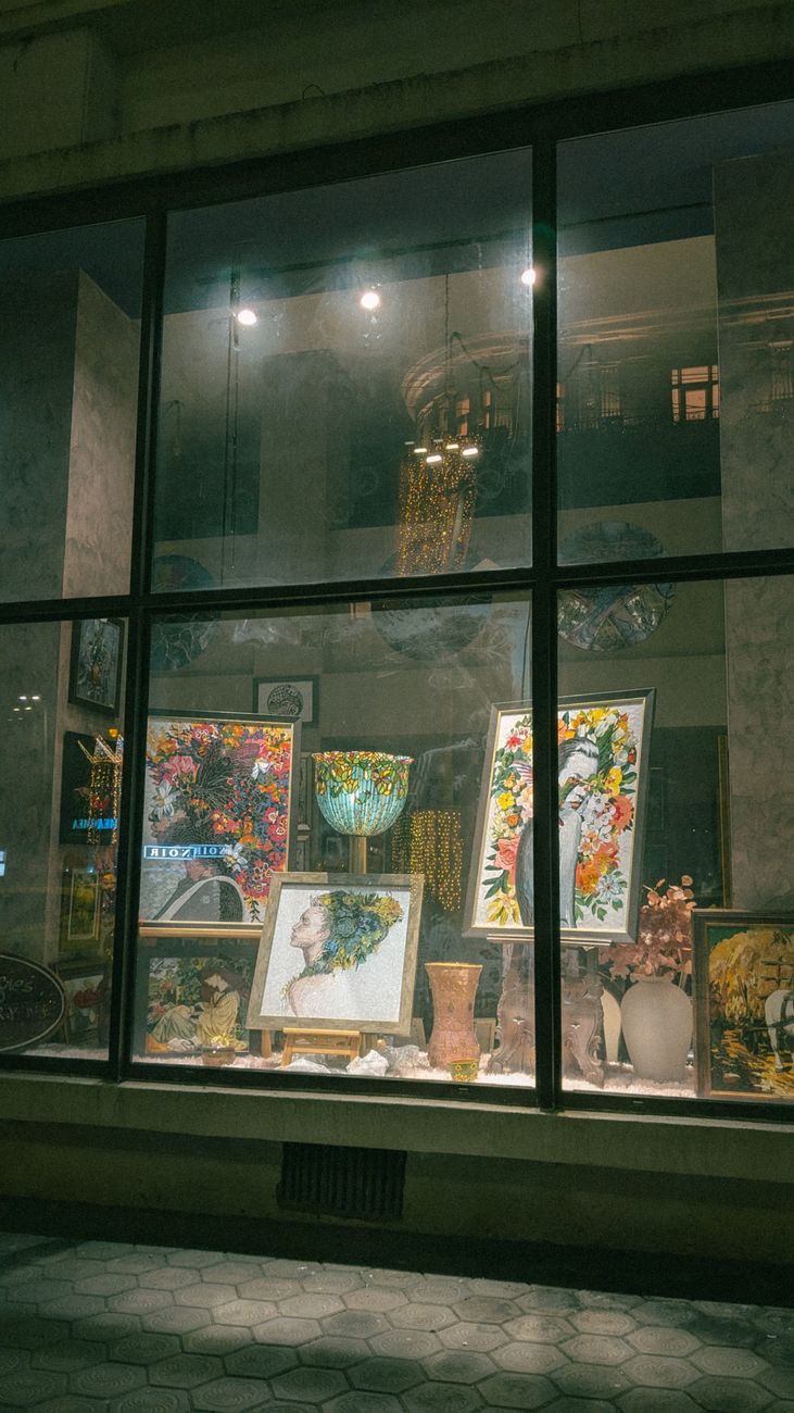 Colorful paintings and ceramics displayed in a shop window at night