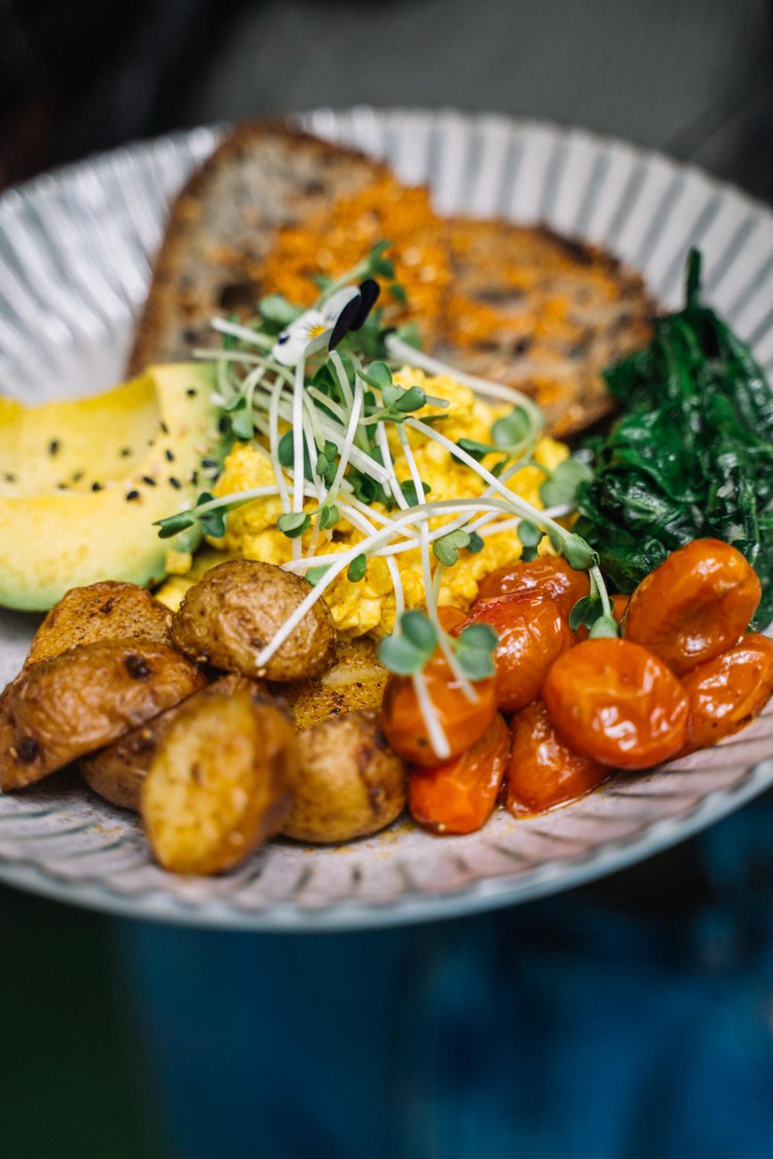 A colorful breakfast plate with eggs, potatoes, tomatoes, spinach, and toast
