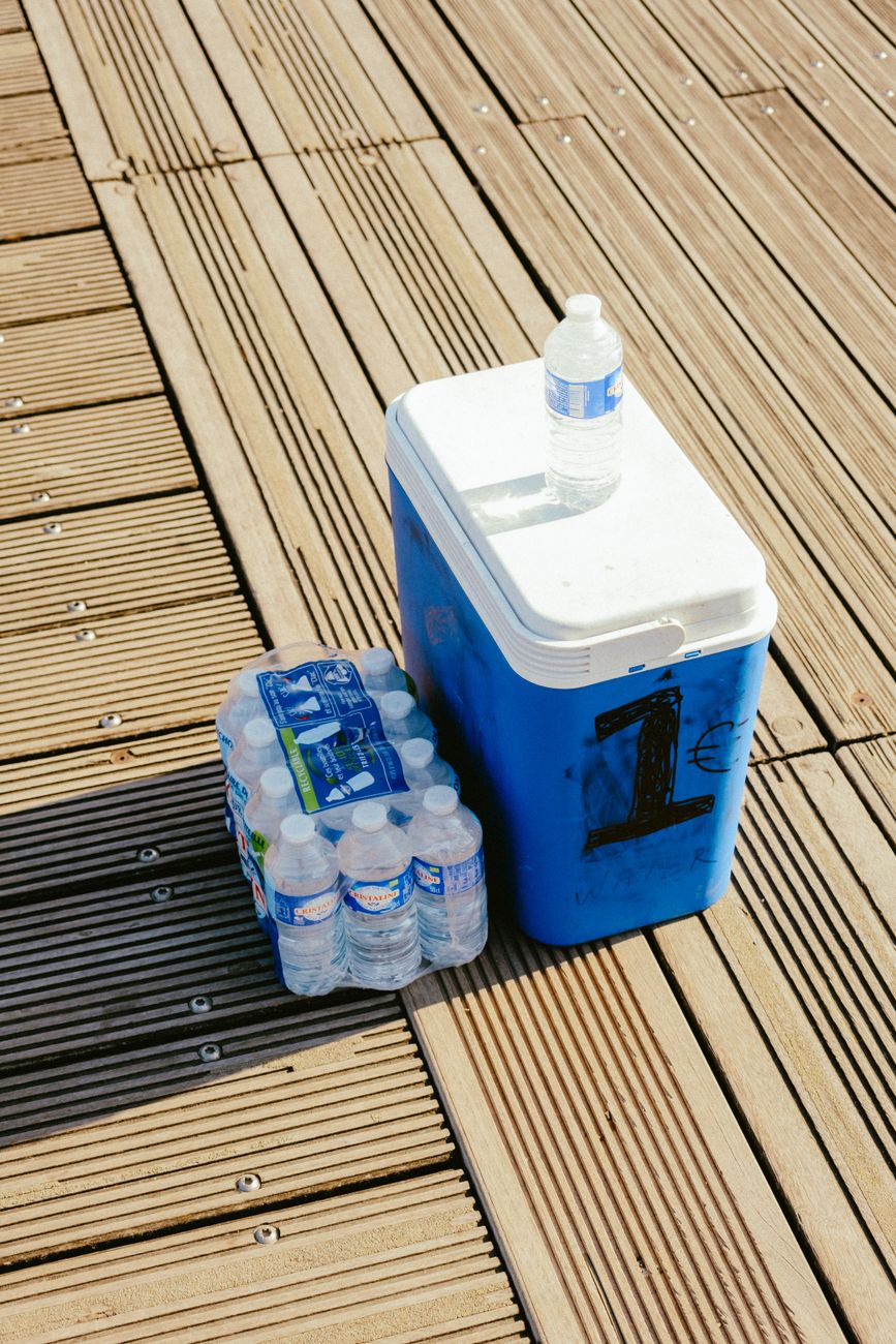 A blue cooler with bottled water on a sunlit wooden deck