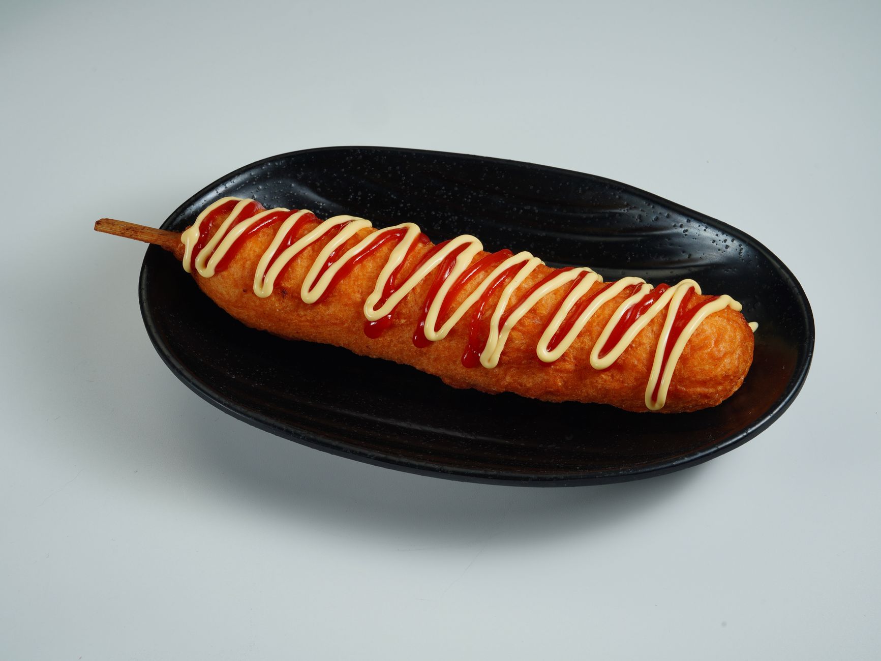 A perfectly cooked corn dog topped with ketchup and mayonnaise