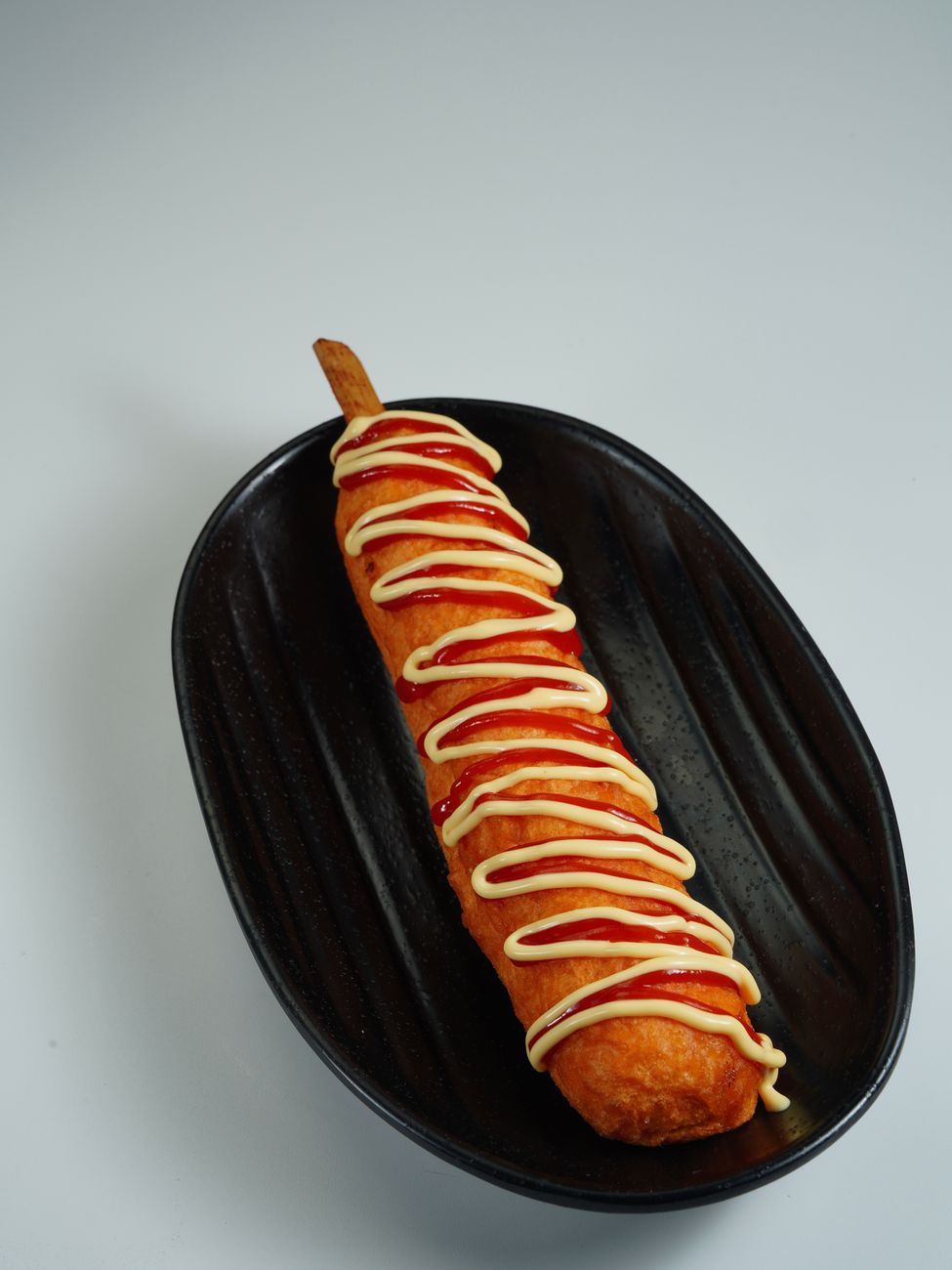 A crispy corn dog drizzled with ketchup and mustard
