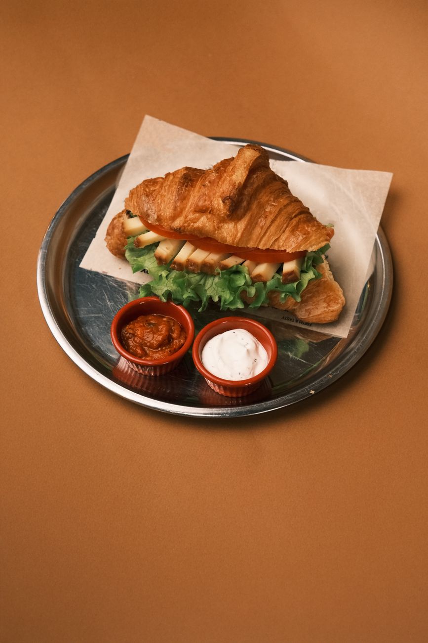 A croissant sandwich served with dips on a serving tray