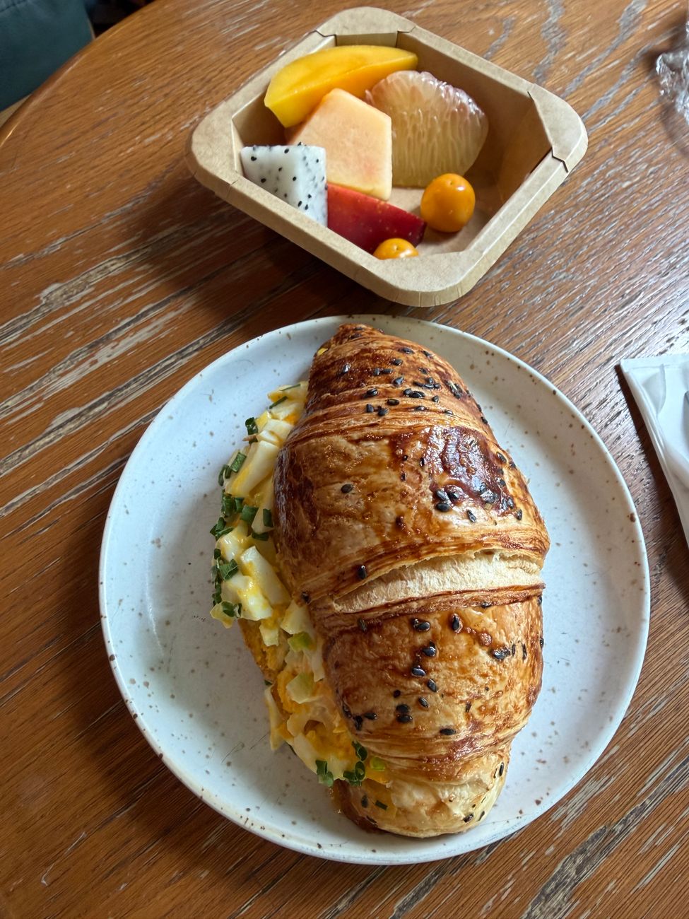A croissant sandwich served with a side of fresh fruit