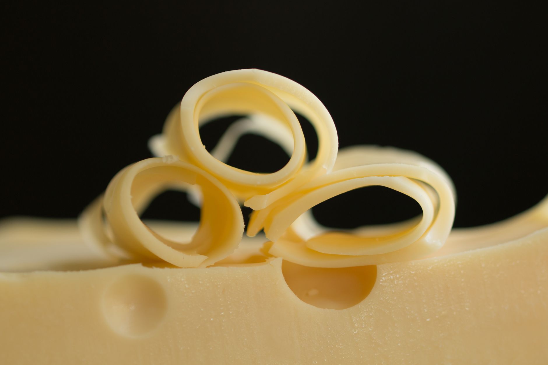 Detailed close-up of curly Swiss cheese slices on a black background