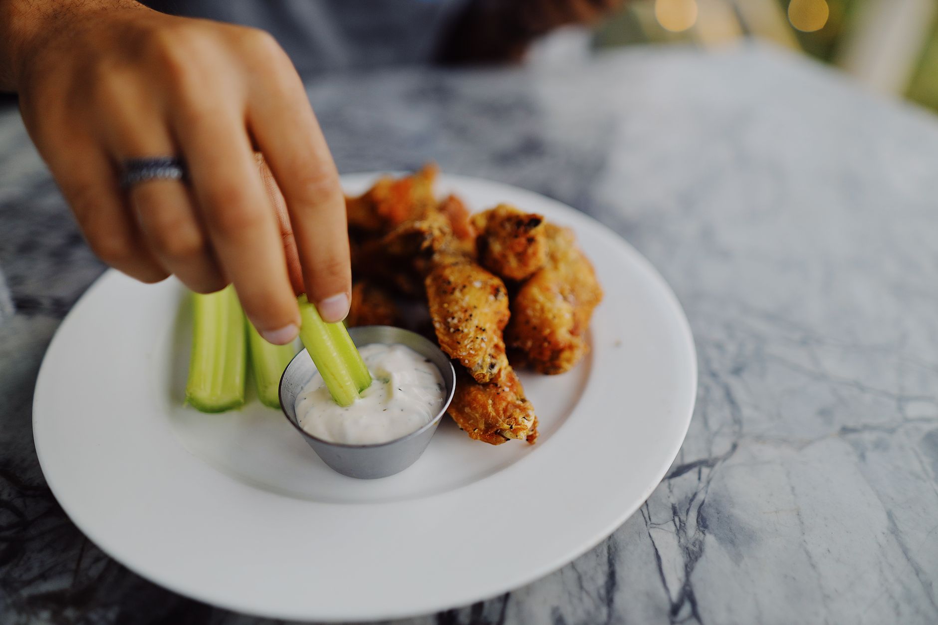 A person dipping fresh celery sticks into a bowl of ranch dip