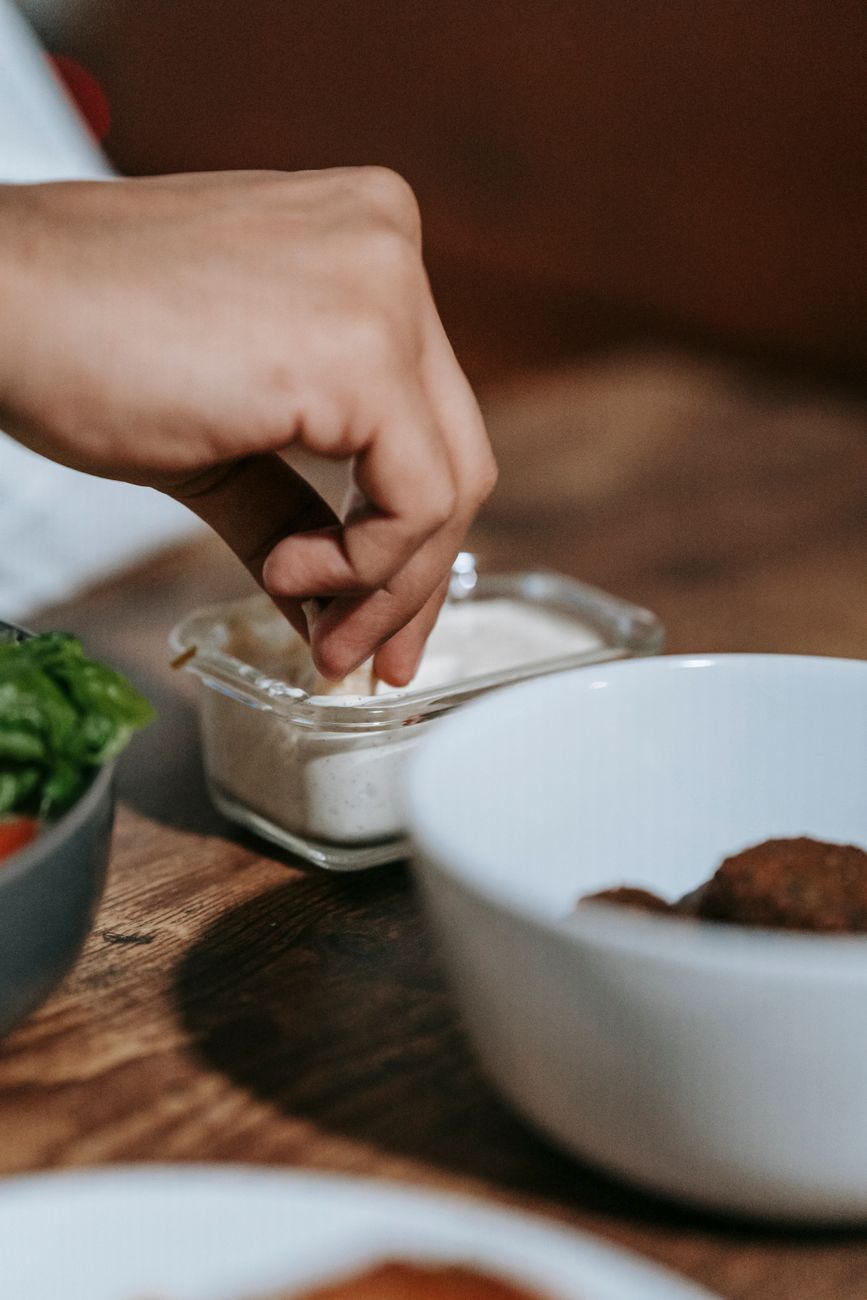 A person dipping food into a creamy white ranch-style sauce