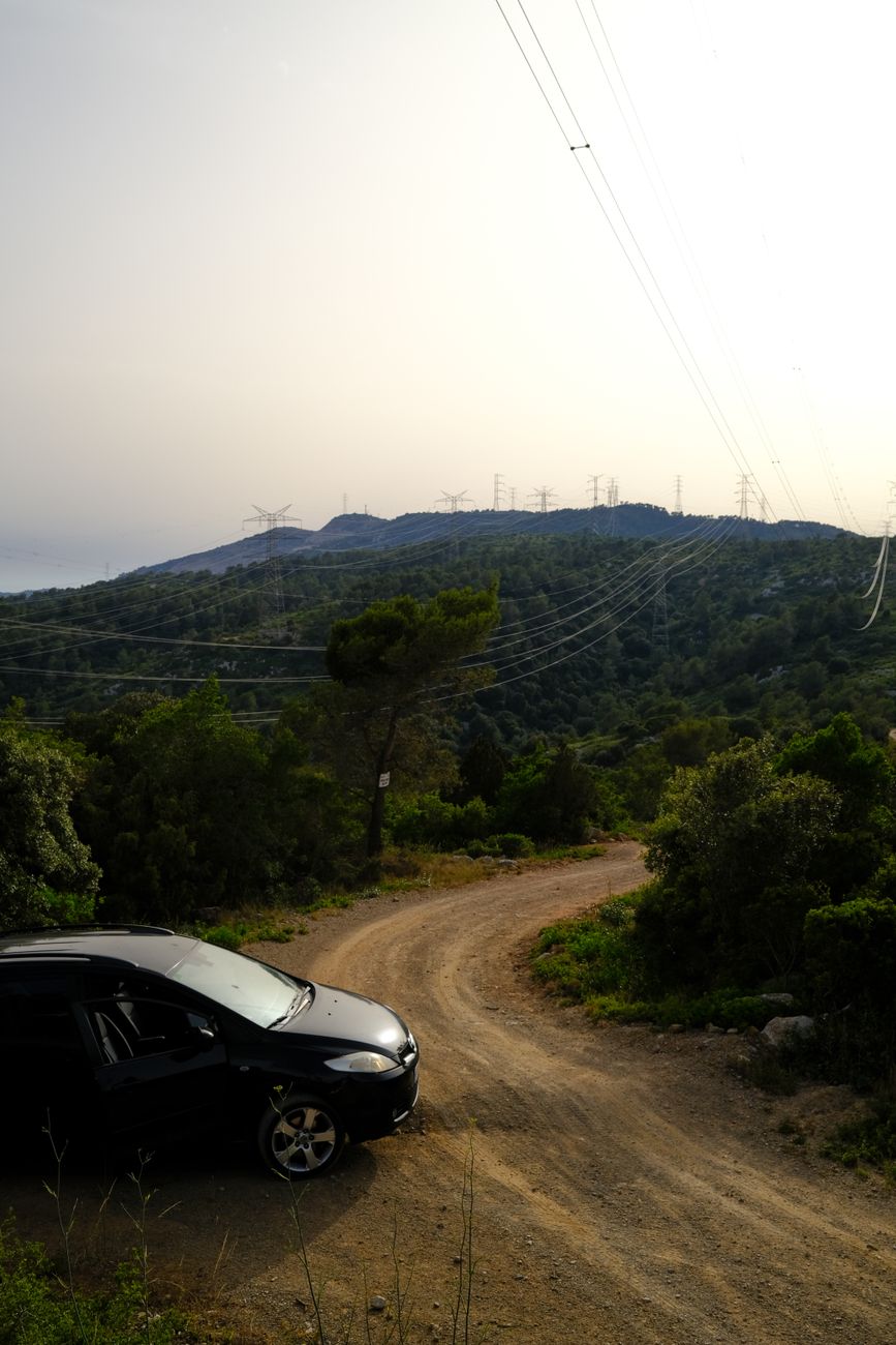 A scenic dirt road through a lush mountain landscape with a parked car