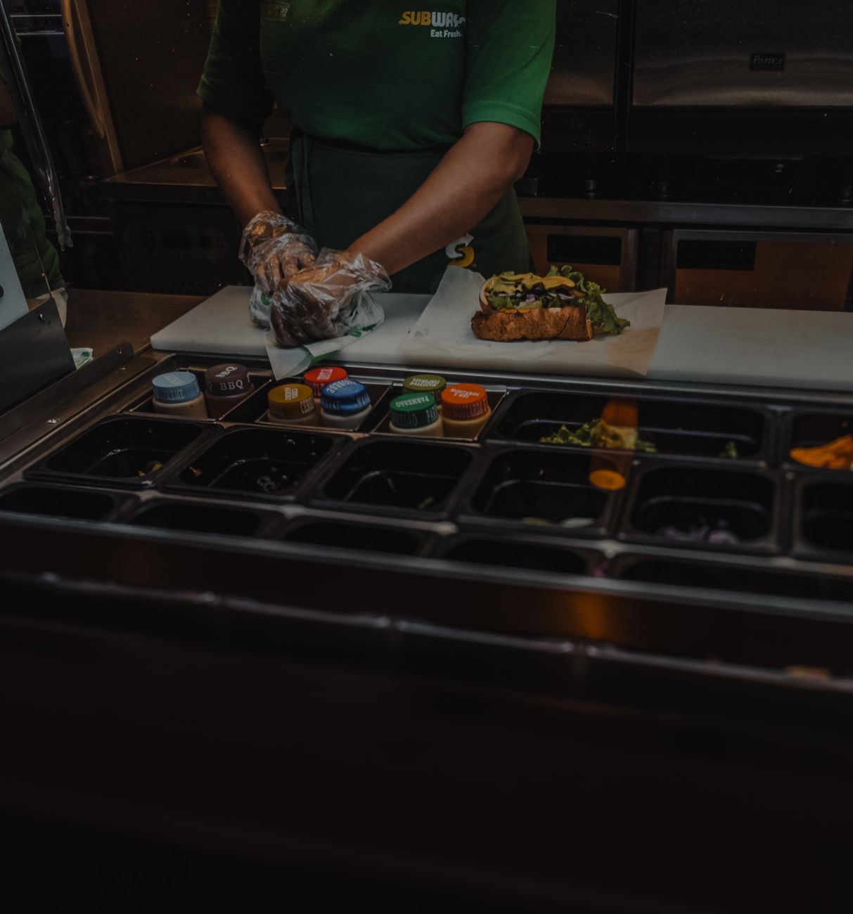 An employee prepares a fresh sandwich with various ingredients