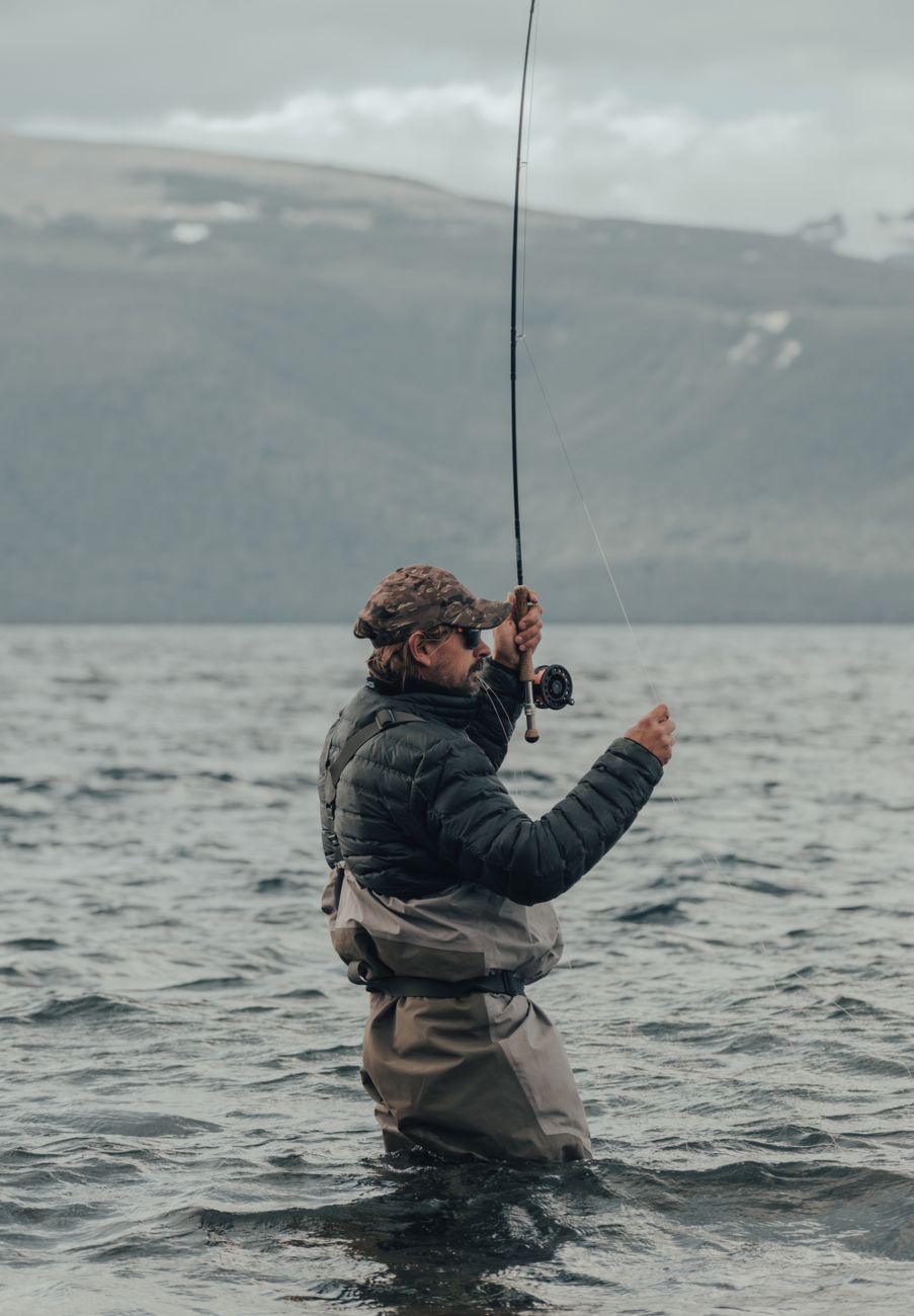 An adult fly fisherman standing knee-deep in a mountain lake, casting a line