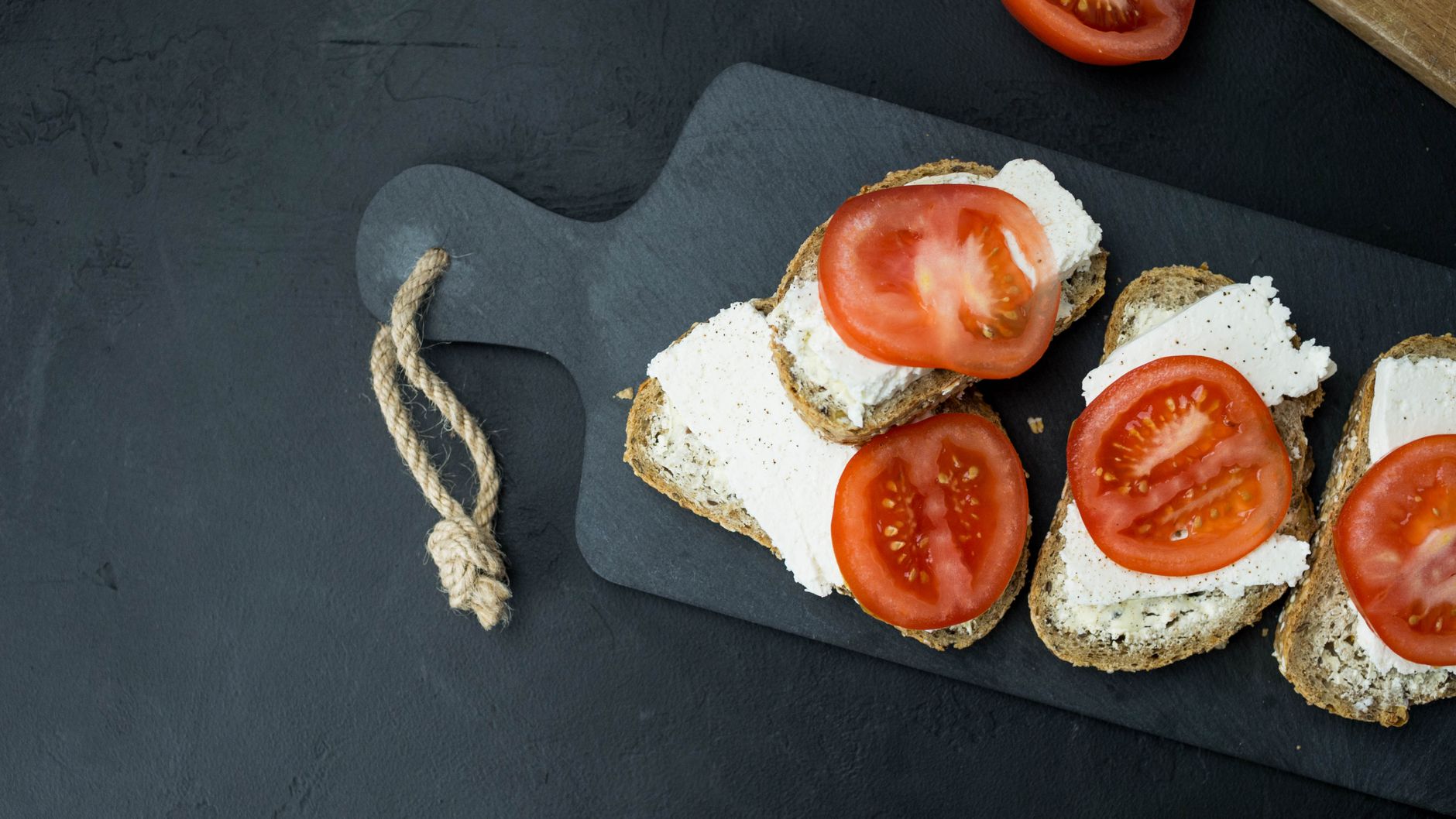 Delicious fresh sandwiches with cream cheese and tomato slices on a cutting board