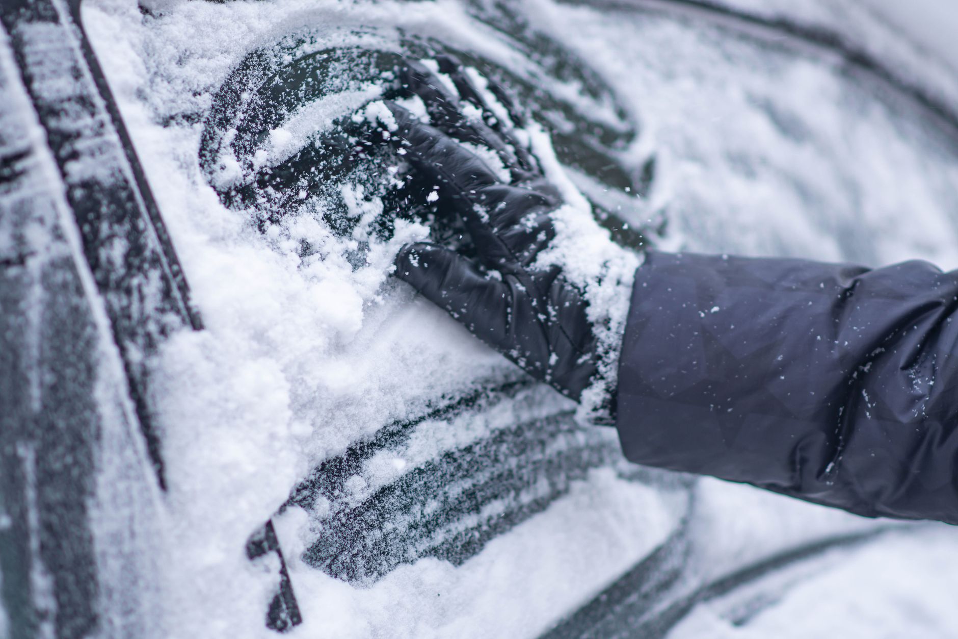 A close-up of a gloved hand clearing snow from a car window during winter