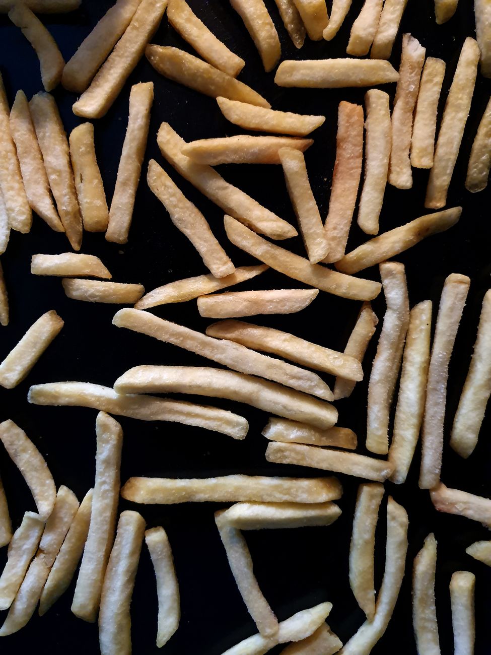 A high-angle shot of golden French fries scattered on a black surface