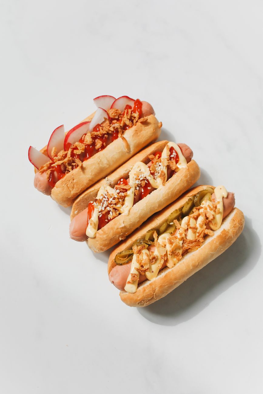 Three gourmet hot dogs with creative toppings on a white background