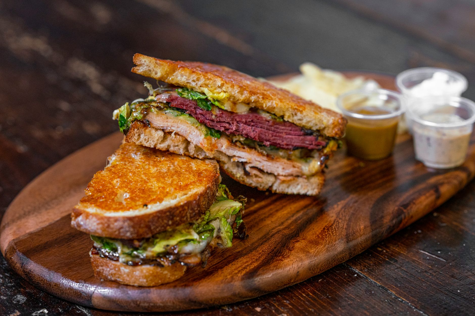 A gourmet sandwich with layers of meats and vegetables on a wooden board