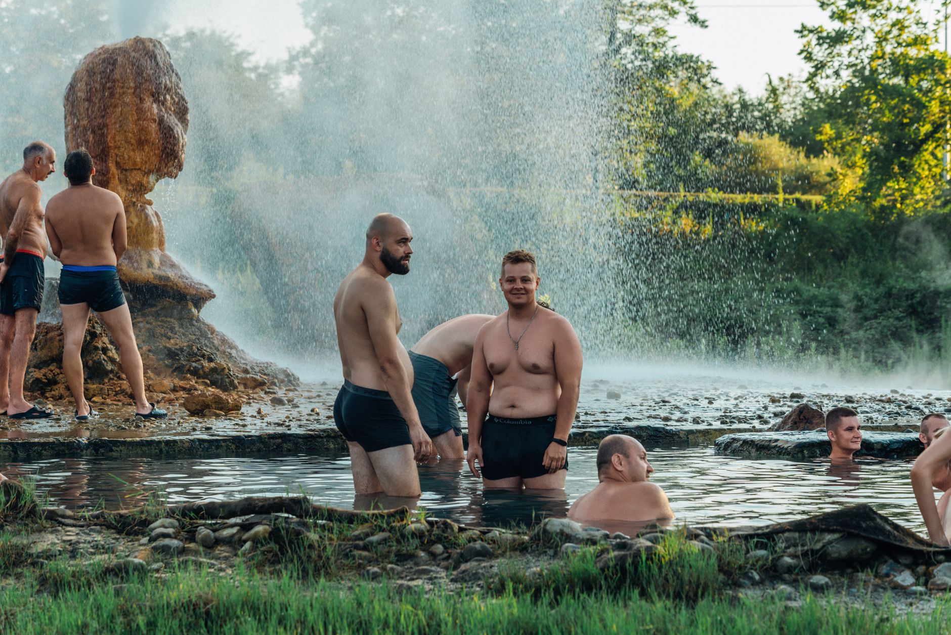 Group of people enjoying natural hot springs outdoors with steam rising
