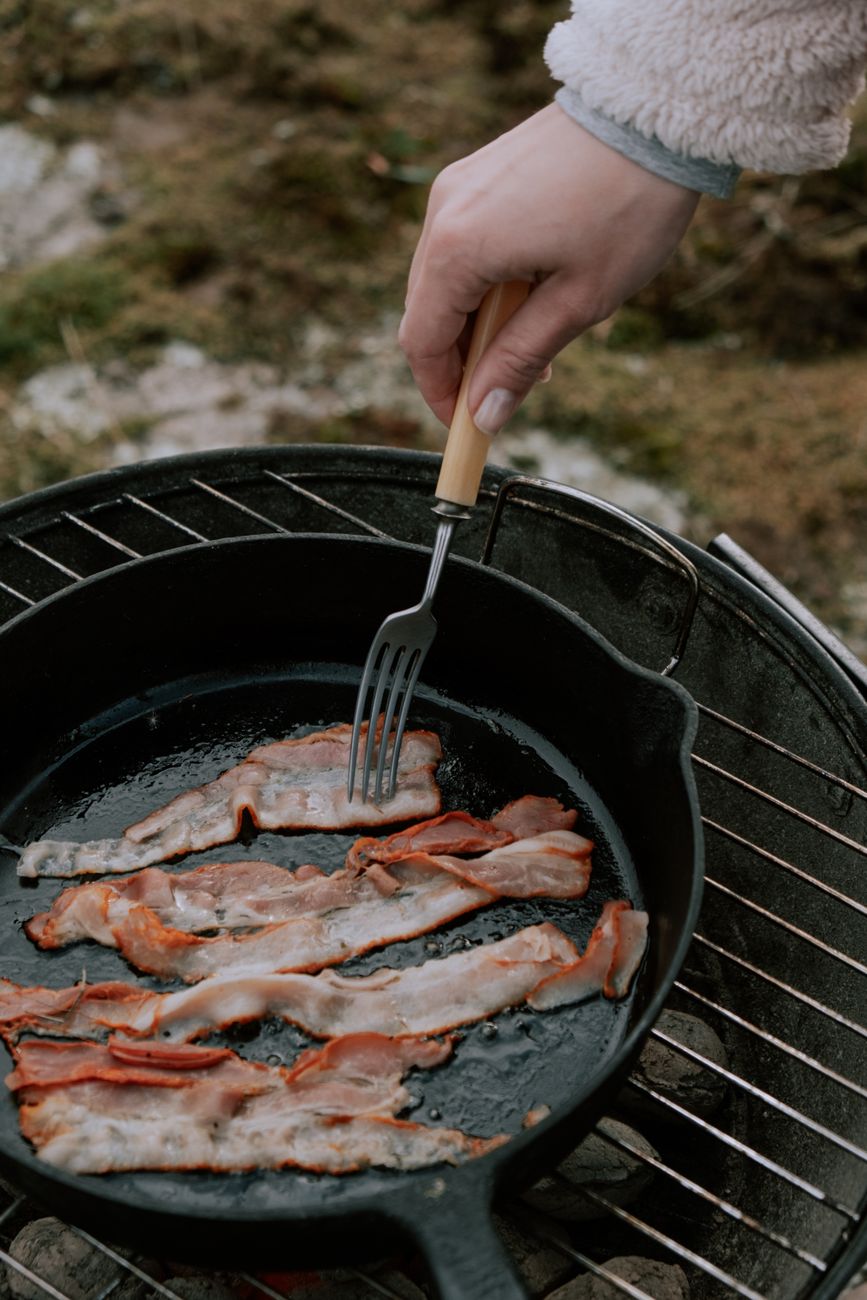 A hand cooking strips of bacon in a hot frying pan