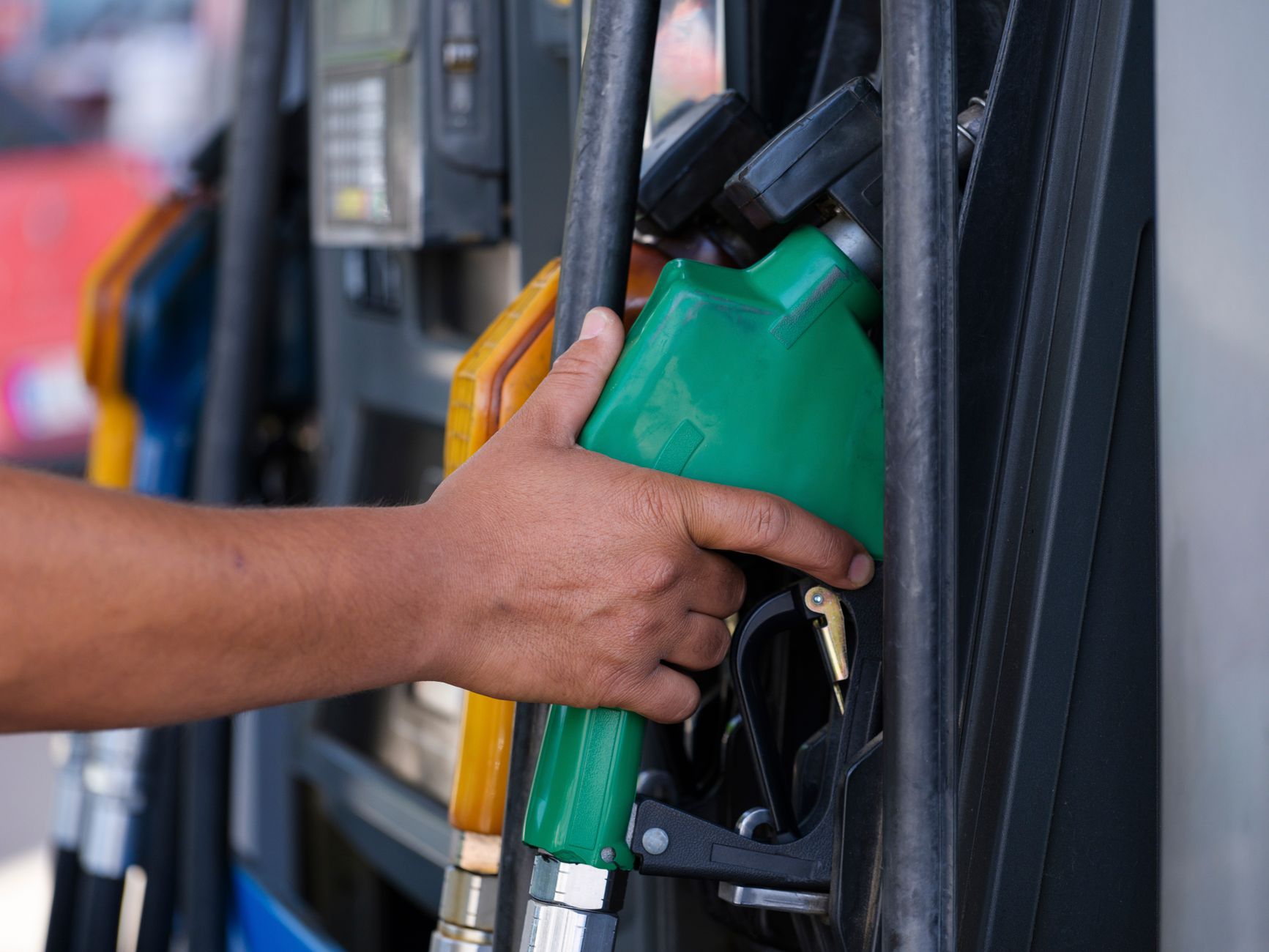 Close-up of a hand holding a green fuel nozzle at a gas pump station