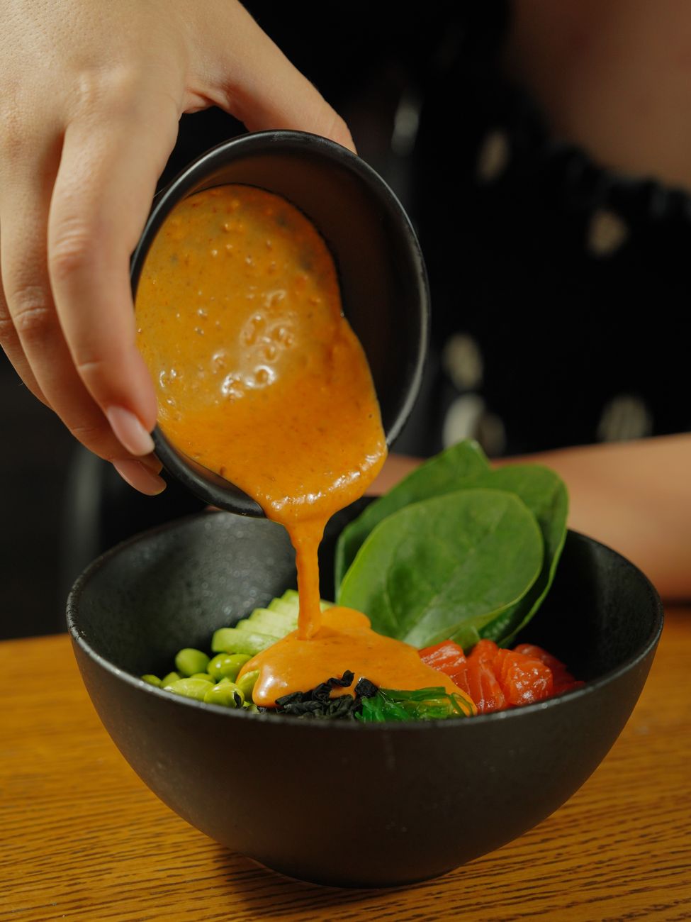 A close-up shot of a hand pouring creamy dressing on a fresh vegetable salad