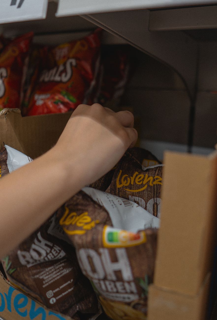Hand reaching for a bag of chips in a convenience store aisle