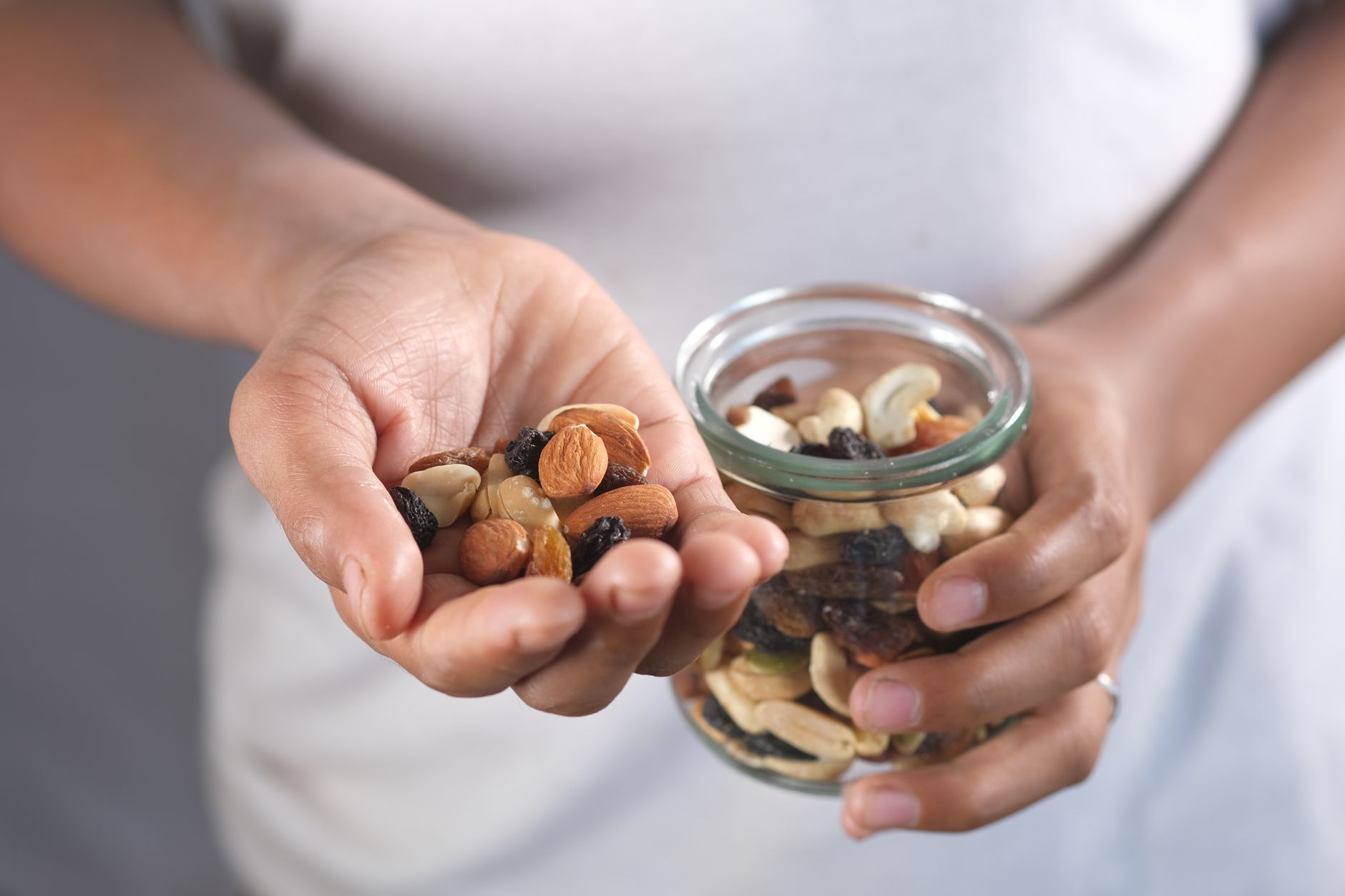 A person’s hands holding a glass jar and a handful of assorted nuts