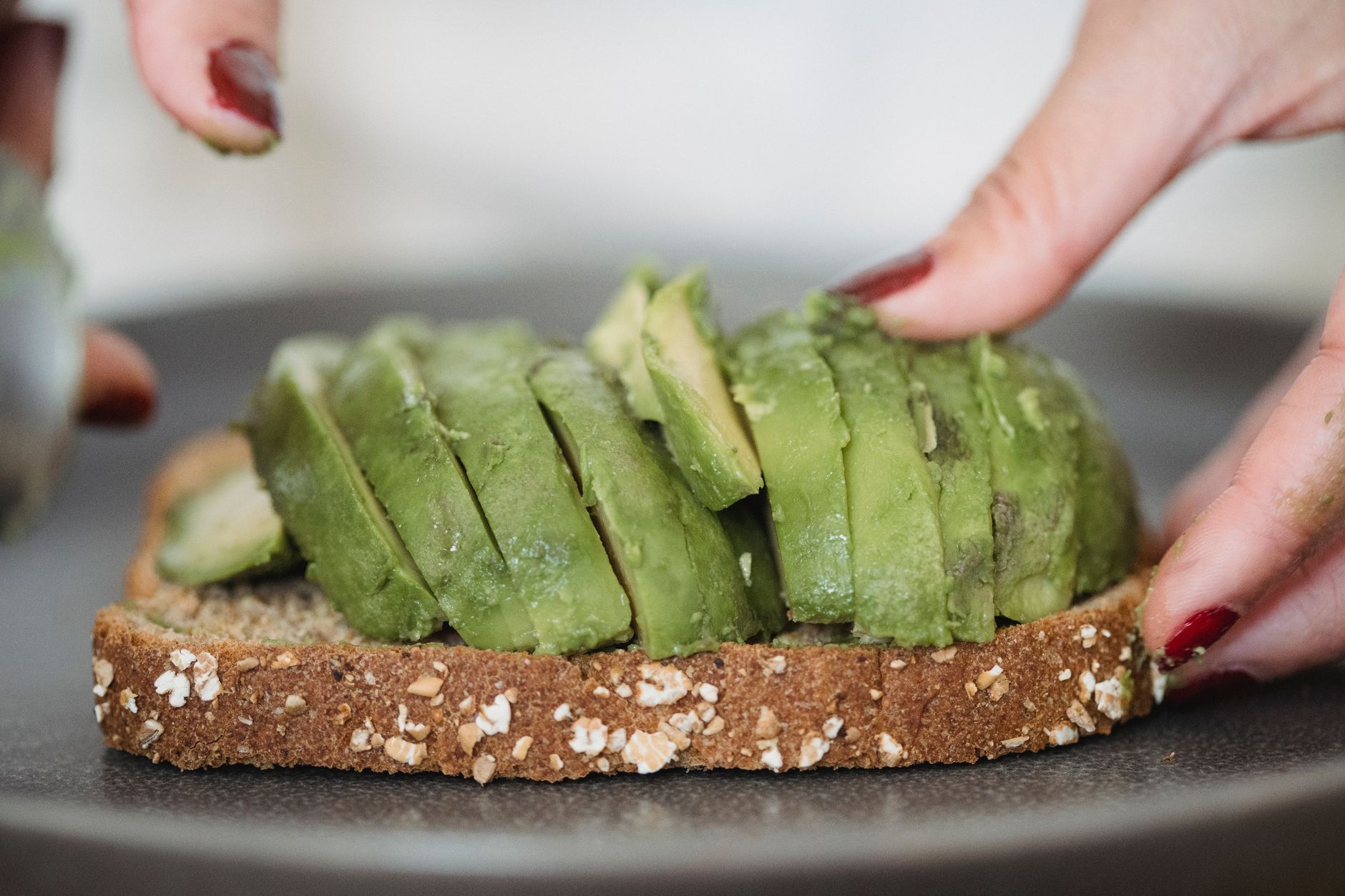 Hands placing avocado slices on whole grain toast for a healthy snack