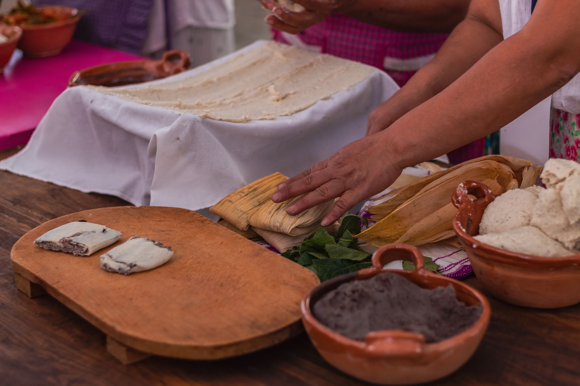 Close-up of hands preparing traditional Mexican tamales with dough and husks